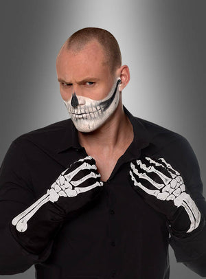 Eine Person in einem schwarzen Shirt trägt schwarze Skeletthandschuhe für Erwachsene in den Größen S–M und hat ein Totenkopf-Gesichts-Make-up; sie steht vor einem grauen Hintergrund mit Farbverlauf.