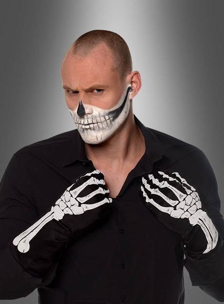 Eine Person in einem schwarzen Shirt trägt schwarze Skeletthandschuhe für Erwachsene in den Größen S–M und hat ein Totenkopf-Gesichts-Make-up; sie steht vor einem grauen Hintergrund mit Farbverlauf.