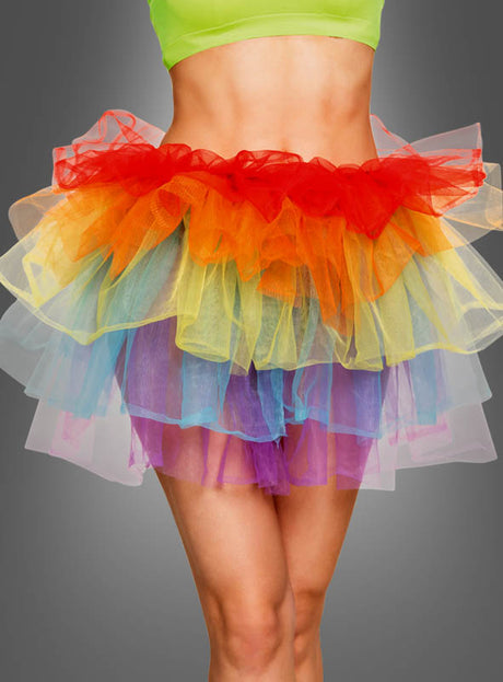 Eine Person, die ein neongrünes Crop-Top und den „Tüll Rock Damen Regenbogen“ trägt – einen mehrlagigen, regenbogenfarbenen Tüllrock mit verspieltem, von Clowns inspiriertem Look –, steht vor einem schlichten grauen Hintergrund.