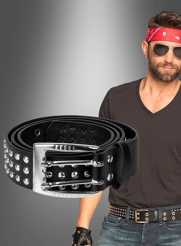 Ein Mann mit rotem Bandana, Sonnenbrille, schwarzem Shirt mit V-Ausschnitt, Nietengürtel und Handschuhen steht hinter einer Nahaufnahme des „Rocker Nietengürtel für Herren 80er Jahre“ – einem auffälligen Punk-Gürtel für Herren mit silberner Schnalle –, der sich als perfektes Accessoire für alle eignet, die ein klares Statement setzen möchten.