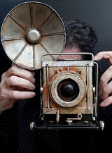 Eine Person, die den „Retro Fotoapparat mit Blitz Deko Kamera“ mit seinem großen runden Blitz nach vorne gerichtet in der Hand hält – ein idealer Vintage-Deko-Akzent für jede 20er-Jahre-Party.