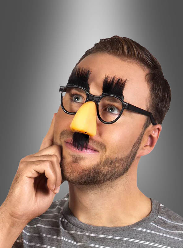 Ein Mann, der die „Brillennase mit buschigen Augenbrauen“ – eine ausgefallene Verkleidung mit falschem Schnurrbart, Brille und einer großen gelben Nase – als lustiges Verkleidungsaccessoire trug, posierte vor einem grauen Hintergrund mit Farbverlauf.