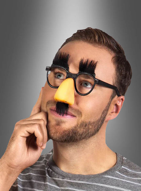 Ein Mann, der die „Brillennase mit buschigen Augenbrauen“ – eine ausgefallene Verkleidung mit falschem Schnurrbart, Brille und einer großen gelben Nase – als lustiges Verkleidungsaccessoire trug, posierte vor einem grauen Hintergrund mit Farbverlauf.