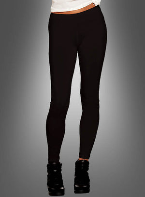 Eine Person ist von der Taille abwärts vor einem grauen Hintergrund mit Farbverlauf zu sehen; sie trägt schwarze Leggings für Damen, schwarze Schuhe und ein weißes Oberteil im 80er-Jahre-Stil.