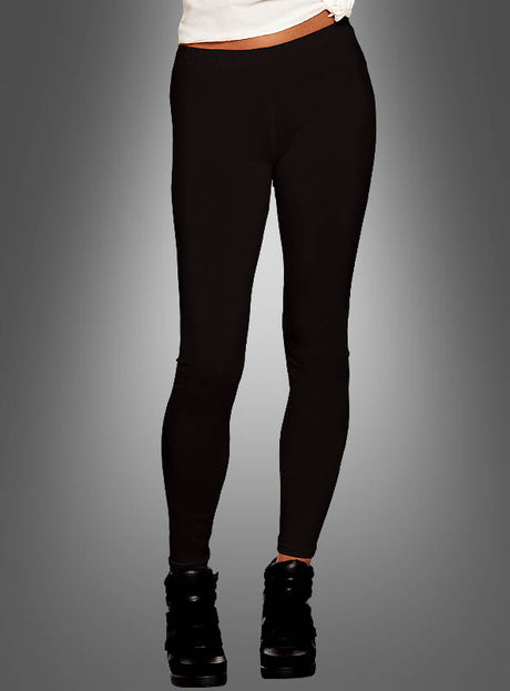 Eine Person ist von der Taille abwärts vor einem grauen Hintergrund mit Farbverlauf zu sehen; sie trägt schwarze Leggings für Damen, schwarze Schuhe und ein weißes Oberteil im 80er-Jahre-Stil.