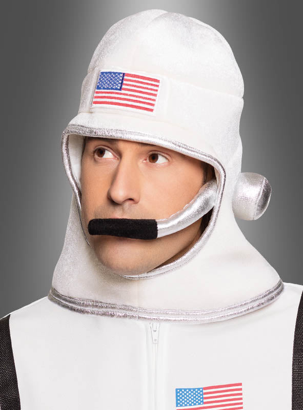 Eine Person, die ein weißes Astronauten-Kostüm mit Aufnähern in Form der amerikanischen Flagge und die charakteristische Raumfahrer-Helmmütze trägt, blickt vor einem grauen Hintergrund mit Farbverlauf leicht nach oben.