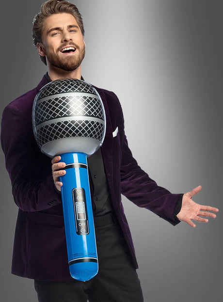 Ein Mann in einem violetten Blazer hält das „Riesiges Mikrofon 76 cm aufblasbar“ vor einem grauen Hintergrund in der Hand und singt hinein – der perfekte Look für jedes Karnevalskostüm.