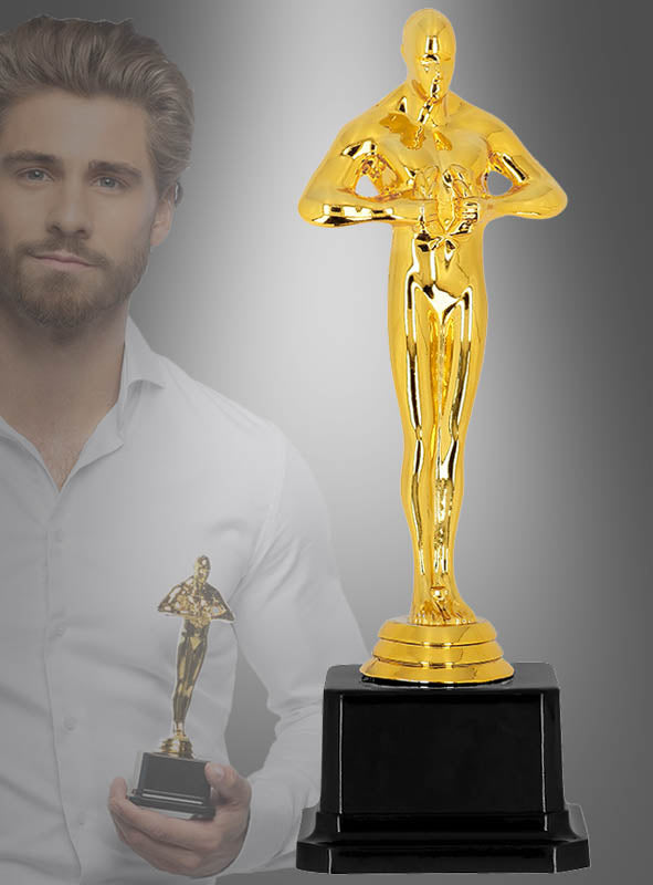 Im Vordergrund steht eine „Goldene Trophäe 21 cm Hollywood Gewinner“ prominent auf einem schwarzen Sockel, während im Hintergrund eine Person, die eine identische Trophäe in der Hand hält – möglicherweise um ihren Gewinn zu feiern –, leicht verblasst erscheint.
