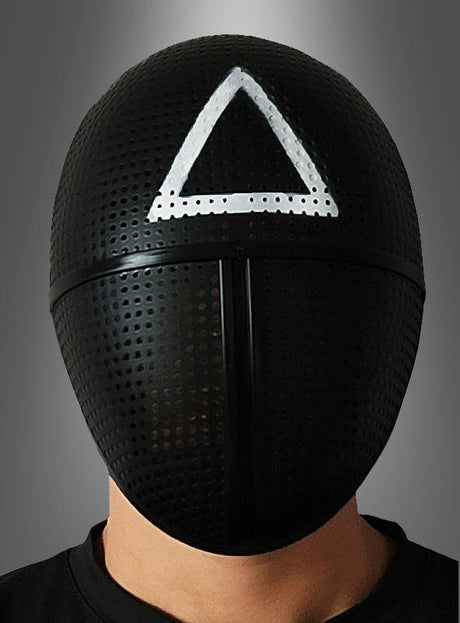 Eine Person, die die schwarze „Game Soldat“-Maske mit Dreieck trägt – inspiriert von der Fernsehserie „Squid Game“ –, steht vor einem grauen Hintergrund. Diese Maske zeichnet sich durch ein schwarzes, perforiertes Design mit einem auffälligen weißen Dreieckssymbol auf der Stirn aus und eignet sich somit ideal für jedes „Tintenfisch-Spiel“-Kostüm.