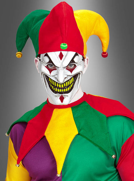 Eine Person trägt das farbenfrohe Unisex-Kostümset „Narrenkappe und Kragen“, komplett mit einer gruseligen Maske mit breitem, zahnigem Grinsen, weißer Gesichtsbemalung sowie gelben und grünen Akzenten. Das auffällige Ensemble umfasst den klassischen Narrenkragen und die leuchtende Kappe, alles vor einem grauen Hintergrund mit Farbverlauf.