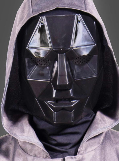 Eine Person, die die „Schwarze Frontmann“-Maske eines mysteriösen Spielleiters und ein graues Kapuzengewand trägt, blickt vor einem schlichten Hintergrund nach vorne.