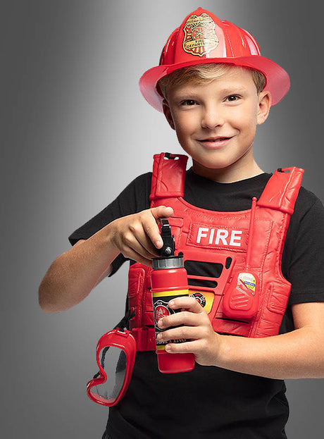 Ein lächelndes Kind, das das Feuerwehrmann-Kostüm-Set für Kinder trägt, bestehend aus einem roten Feuerwehrhelm und einer Weste, hält in einer Hand einen Spielzeugfeuerlöscher, während an seiner Seite eine Schutzbrille hängt.