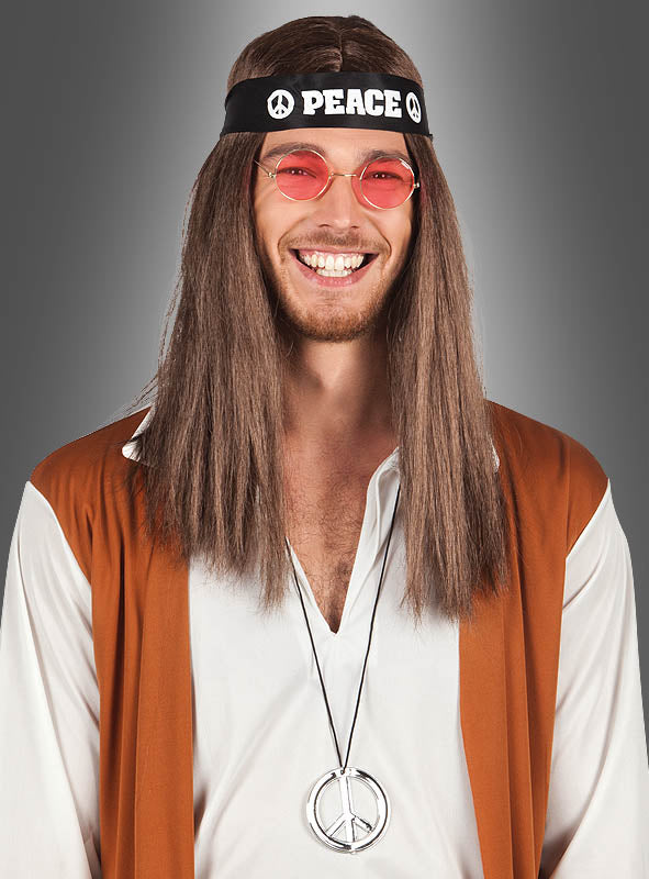 Vor einem grauen Hintergrund ist eine lächelnde Person mit langen braunen Haaren zu sehen, die eine runde rosa Brille, ein PEACE-Stirnband aus dem „Hippie Peace Set für Kinder und Erwachsene“, ein weißes Hemd, eine braune Weste und eine Halskette mit einem Peace-Symbol trägt.