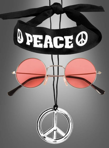 Das „Hippie-Peace-Set für Kinder und Erwachsene“ besteht aus einem schwarzen Stirnband mit der Aufschrift „PEACE“ und Friedenssymbolen, einer runden rosa Sonnenbrille und einer großen silbernen Halskette mit Friedenssymbol – Flower-Power-Accessoires, die hier wunderschön vor einem grauen Hintergrund zur Geltung kommen.