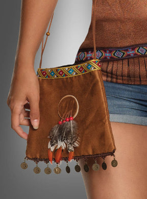 Eine Person hält die „Indianer-Handtasche mit Traumfänger“ in der Hand – eine braune Wildleder-Handtasche mit Perlenbesatz, Federn, roten Perlen, Münzanhängern und einem Traumfänger-Detail –, die an einem langen Riemen getragen und mit einem braunen Oberteil und Jeansshorts kombiniert wird – das perfekte Accessoire, um jedes Wildwest-Kostüm abzurunden.