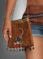 Eine Person hält die „Indianer-Handtasche mit Traumfänger“ in der Hand – eine braune Wildleder-Handtasche mit Perlenbesatz, Federn, roten Perlen, Münzanhängern und einem Traumfänger-Detail –, die an einem langen Riemen getragen und mit einem braunen Oberteil und Jeansshorts kombiniert wird – das perfekte Accessoire, um jedes Wildwest-Kostüm abzurunden.