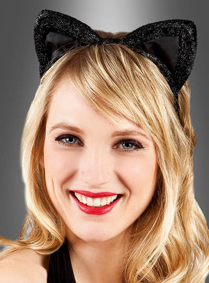 Eine Frau mit blonden Haaren und rotem Lippenstift lächelt vor einem grauen Hintergrund mit Farbverlauf in die Kamera. Sie trägt einen schwarzen, glitzernden Haarreif mit Katzenohren – das perfekte Accessoire für jeden verspielten Katzenkostüm-Look.