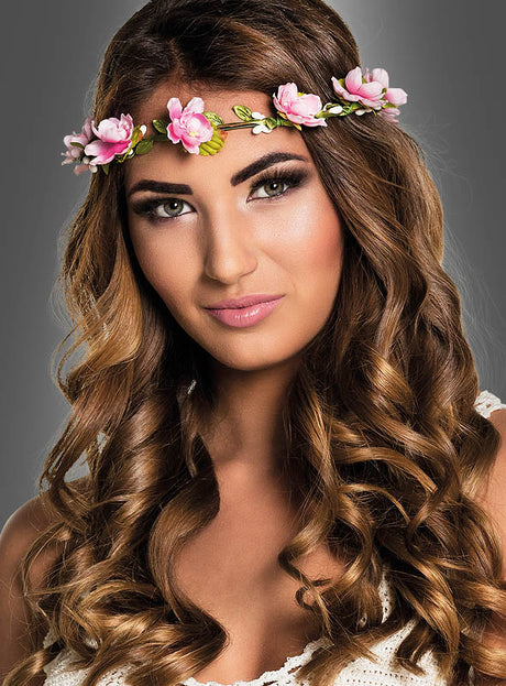 Eine Frau mit langen, welligen braunen Haaren trägt den „Blüten Haarkranz“ in Rosa und ein weißes Oberteil und posiert vor einem neutralen grauen Hintergrund – perfekt für eine Märchen-Mottoparty.