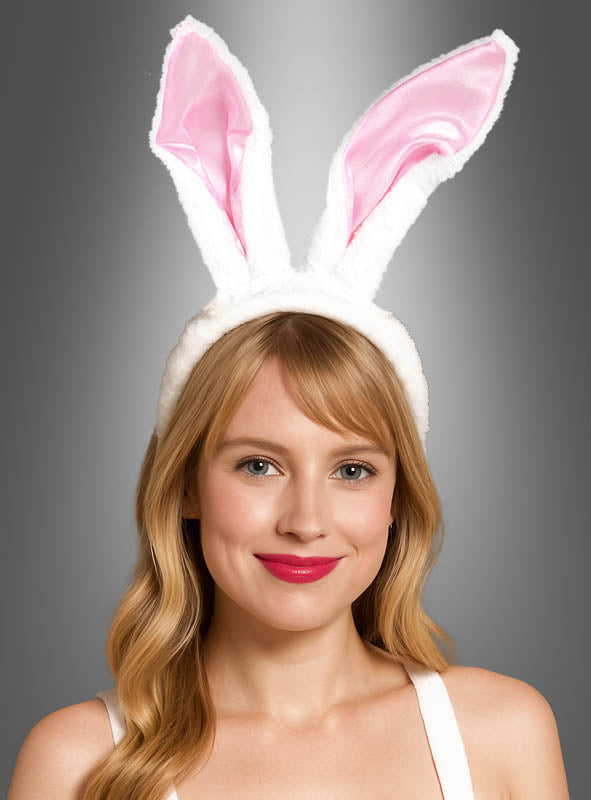 Eine Frau mit blonden Haaren trägt das „Hasenohren-Haarreif Damen“-Modell mit hohen, rosa gefütterten Hasenohren, das vor einem grauen Hintergrund für einen verspielten Hasenkostüm-Look sorgt.