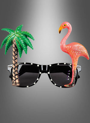 Eine schwarze Sonnenbrille mit einer Palme aus Kunststoff auf der linken Seite und einem rosa Flamingo auf der rechten Seite vor einem grauen Hintergrund mit Farbverlauf – diese verspielte „Strandparty Brille Aloha“ ist perfekt, um jeder Hawaii-Party oder Strandfeier eine fröhliche Atmosphäre zu verleihen.