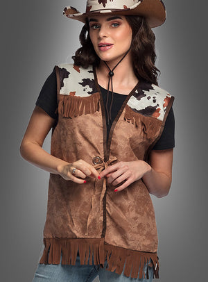 Eine Person, die einen braunen Cowboyhut, ein schwarzes T-Shirt und die „Cowboy Weste für Damen“ mit Kuhmuster an den Schultern trägt, posiert vor einem grauen Hintergrund und sorgt so für einen authentischen Western-Look.