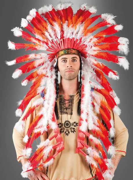 Eine Person, die ein hellbraunes Hemd mit schwarzem Muster und den „Deluxe Häuptling Indianer Federschmuck“-Kopfschmuck mit auffälligen roten, weißen und orangefarbenen Federn trägt, steht vor einem neutralen grauen Hintergrund.