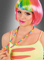 Eine Person mit einer kurzen, bunten Perücke und auffälligem Make-up, die die Halskette „Bunte Perlenkette Regenbogen“ in der Hand hält und ein gelbes Oberteil mit Ausschnitten trägt, vor einem grauen Hintergrund mit Farbverlauf.