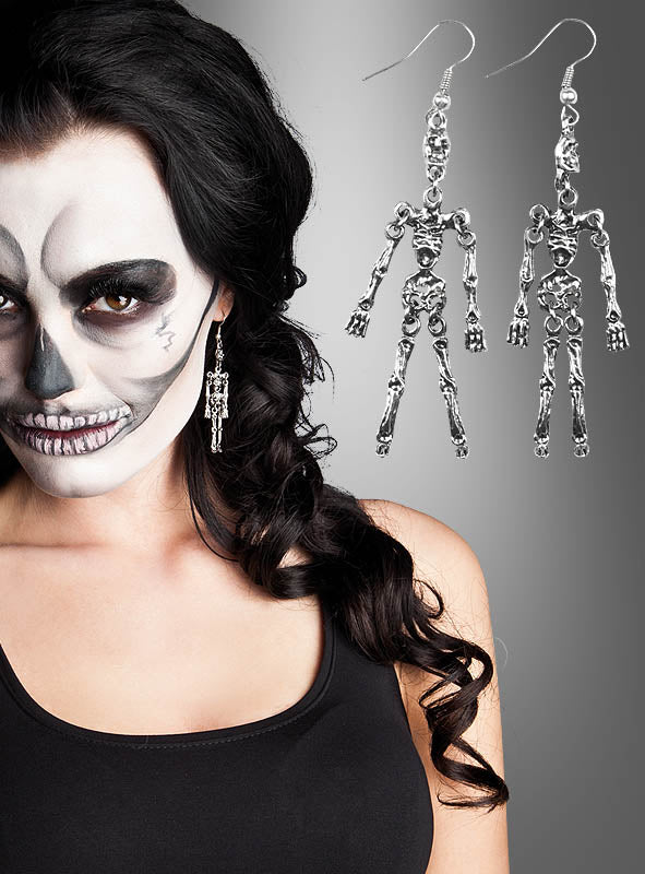 Eine Frau mit Skelett-Gesichtsbemalung trägt ein schwarzes Trägertop und präsentiert den „Ohrringe Skelett“-Halloween-Schmuck – das perfekte Accessoire für Halloween. Rechts ist eine vergrößerte Ansicht der „Ohrringe Skelett“ vor einem grauen Hintergrund mit Farbverlauf zu sehen.