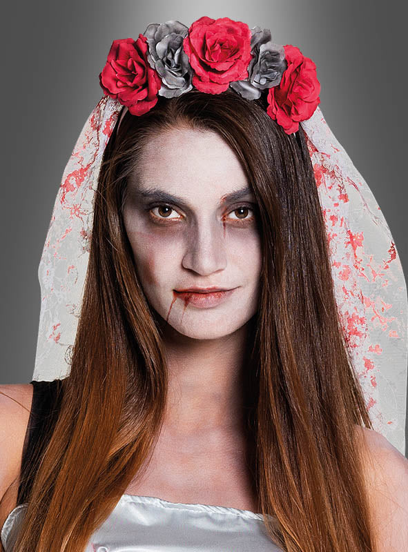 Eine Frau mit langen braunen Haaren in einem weißen Kleid, die ein geblümtes Stirnband und den „Horrorbraut“-Haarschmuck mit Schleier trägt, mit blassem Make-up und dunklen Augen, die an einen Vampir oder eine untote Braut erinnert – ein ideales Halloween-Kostüm.