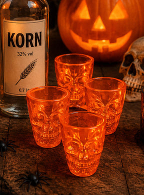 Eine Flasche mit der Aufschrift „Korn“, vier Schnapsgläser mit Totenkopf-Motiv (à 50 ml), ein geschnitzter Kürbis, ein Totenkopf und künstliche Spinnen auf einer Holzunterlage – perfekte Deko-Akzente für deine Halloween-Party.