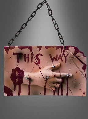 Eine mit Ringen geschmückte Hand hält das „Halloween-Hinweisschild 32 cm – blutige Hand“ fest, ein blutbeflecktes Schild mit der Aufschrift „THIS WAY“ in roter Schrift, das an einer schwarzen Kette vor einem grauen Hintergrund hängt. Dieses gruselige Horrorschild ist die perfekte Halloween-Dekoration, um Ihre Gäste zu den schaurigen Feierlichkeiten zu führen.