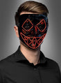Eine Person, die ein schwarzes Hemd und die „LED Killer Maske Purger“ trägt – eine schwarze Maske mit roten LED-Linien, die Augen, Nase und den gezackten Mund umrahmen –, steht vor einem grauen Hintergrund.