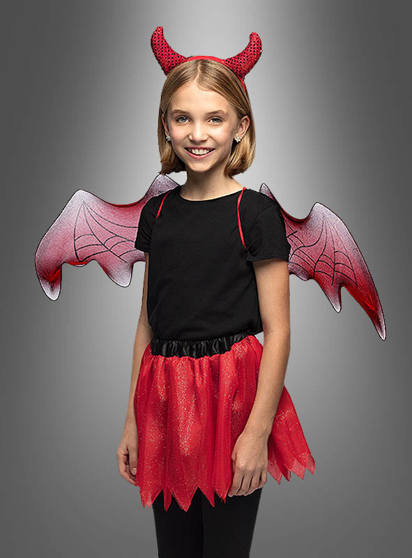 Ein kleines Mädchen steht lächelnd vor einem grauen Hintergrund mit Farbverlauf und trägt das „Teufel“-Kostüm-Set für Kinder, bestehend aus einem schwarzen Shirt, einem roten Rock, roten Teufelshörnern und roten Fledermausflügeln. Dieses bezaubernde Halloween-Kostüm für Mädchen verleiht jeder festlichen Feier eine verspielte Note.
