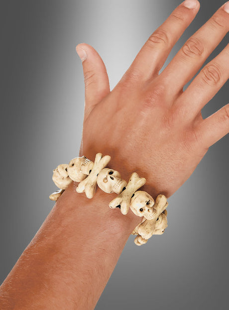 Eine Hand, die das „Cooles Voodoo Totenkopf“-Armband trägt, gefertigt aus knochenähnlichen Perlen in Form von Totenköpfen und gekreuzten Knochen, vor einem grauen Farbverlaufshintergrund – ideal, um jedes Piratenkostüm oder Halloween-Kostüm abzurunden.