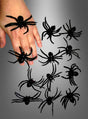 Eine Hand, auf der mehrere „Schwarze Spinnen aus Gummi“ (6 cm) aus der 12er-Packung liegen, umgeben von weiteren identischen Spinnenspielzeugen auf grauem Hintergrund – perfekt als Halloween-Dekoration.