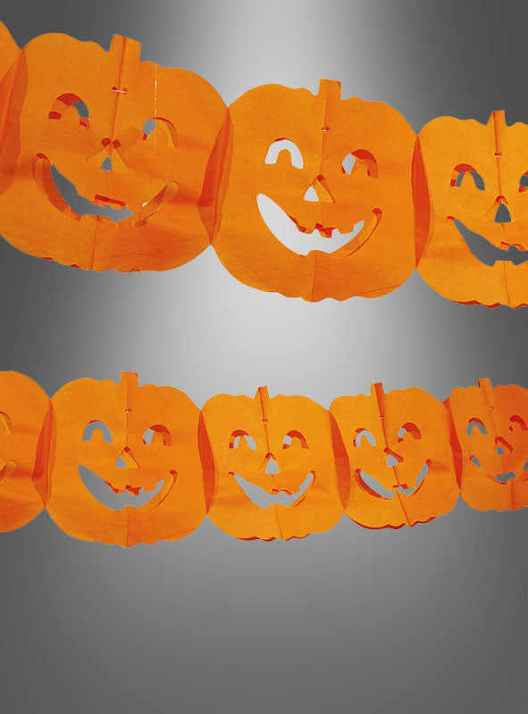 Kürbis-Papiergirlande zu Halloween aus orangefarbenem Papier mit wiederkehrenden Jack-o-Lantern-Motiven, präsentiert vor einem neutral-grauen Hintergrund – ideal als auffällige Herbstdekoration für deine Halloween-Party.