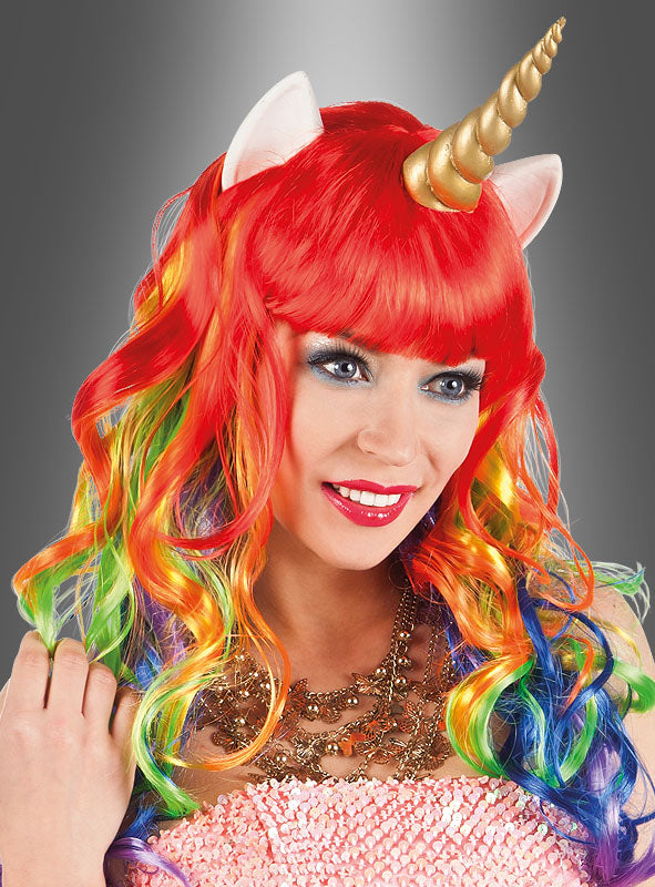 Eine Person lächelt vor einem grauen Hintergrund und trägt die „Einhorn-Perücke für Damen“ – eine leuchtend rote Perücke in Regenbogenfarben mit einem Einhornhorn und weißen Ohren –, die den Zauber eines idealen Einhornkostüms perfekt einfängt.