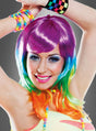 Eine lächelnde Person, die die „Regenbogen“-Damenperücke trägt, mit auffälligem Make-up und Accessoires aus Perlen, posiert mit erhobenen Armen vor einem grauen Hintergrund.