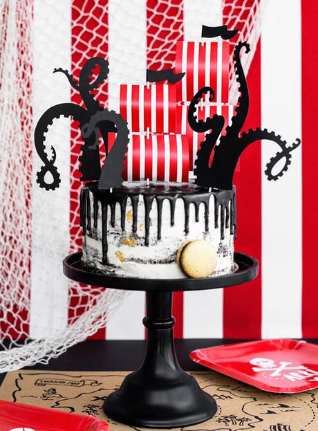 Schwarz-weißer Kuchen mit schwarzen Tentakel-Dekorationen, rot-weiß gestreiften Kerzen und einem Keks auf einem schwarzen Ständer; rot-weiß gestreifter Hintergrund – ideal, um die „Tortendeko Piratenparty Tentakel-Set-Muffins“ oder andere „Kuchendeko Piratenparty“-Elemente bei deiner nächsten Piraten-Kindergeburtstagsfeier einzusetzen.