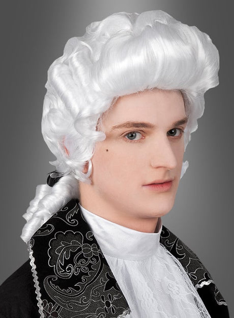 Ein junger Mensch mit einer weißen Barockperücke für Herren und Kleidung im Stil des 18. Jahrhunderts, der mit neutralem Gesichtsausdruck leicht nach rechts blickt, vor einem grauen Hintergrund.