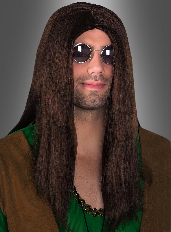 Ein Mann mit langen braunen Haaren, die wie eine Hippie-John-Langhaarperücke frisiert sind, einer runden Sonnenbrille und einem grün-braunen 70er-Jahre-Kostüm posiert vor einem grauen Hintergrund.