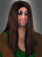 Ein Mann mit langen braunen Haaren, die wie eine Hippie-John-Langhaarperücke frisiert sind, einer runden Sonnenbrille und einem grün-braunen 70er-Jahre-Kostüm posiert vor einem grauen Hintergrund.