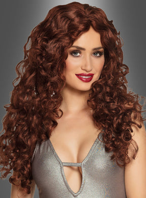 Eine Frau mit langen, lockigen, rotbraunen Haaren, die ein silbernes Oberteil trägt und vor einem grauen Hintergrund mit Farbverlauf posiert und lächelt – perfekt, um einen Karnevalslook zu präsentieren oder die rotbraune Langhaar-Lockenperücke in Szene zu setzen.