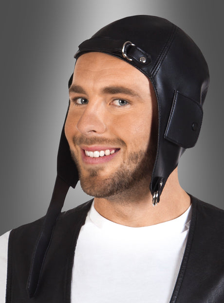 Ein Mann, der die „Fliegerhaube Pilot für Erwachsene“ – eine schwarze Lederkappe im Fliegerstil – sowie ein weißes Hemd und eine schwarze Weste trägt, lächelt vor einem grauen Hintergrund mit Farbverlauf und bildet damit eine ideale Ergänzung für jede Steampunk-Kostüm-Accessoire-Kollektion.