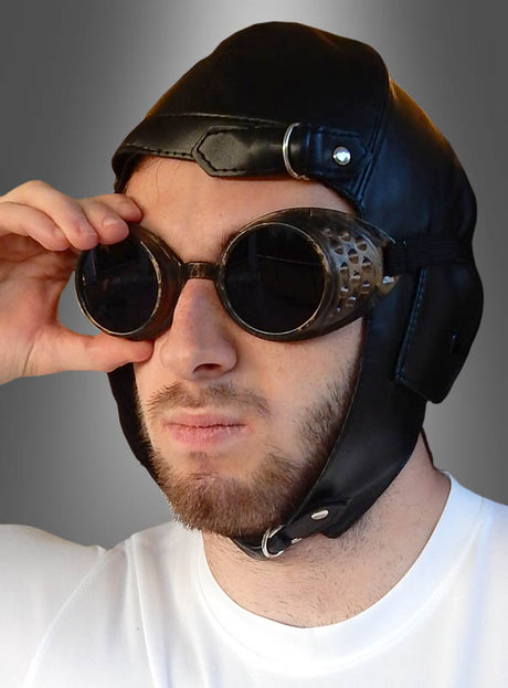 Ein Mann, der die „Fliegerhaube Pilot für Erwachsene“ trägt – einen Vintage-Fliegerhelm aus Leder in Kombination mit einer runden Schutzbrille –, rückt seine Brille zurecht, während er vor einem grau verlaufenden Hintergrund nach vorne blickt. Dieser klassische Look ist vom Steampunk-Stil inspiriert und damit das perfekte Steampunk-Kostüm-Accessoire für alle, die zeitlose Abenteuer und einen markanten Charakter suchen.