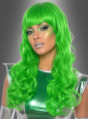 Eine Person mit langen, welligen, neongrünen Haaren, gestylt mit der „Lange Lockenperücke Alien grün“, und auffälligem Metallic-Make-up, die ein glänzendes grün-silbernes Outfit trägt, das an eine Meerjungfrau erinnert, und vor einem grauen Hintergrund mit Farbverlauf posiert.
