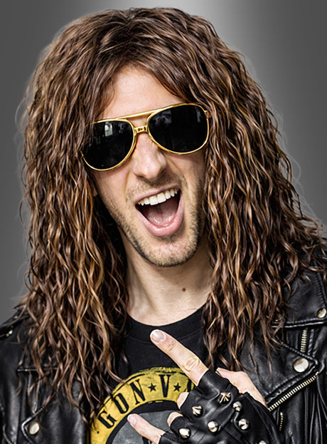 Ein Mann mit langen, lockigen Haaren, die zu einer braunen 80er-Jahre-Rocker-Perücke frisiert sind, trägt eine Sonnenbrille, eine schwarze Lederjacke und fingerlose Handschuhe. Er macht eine Rocker-Geste und lächelt mit offenem Mund.
