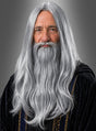 Ein älterer Mann mit langem grauen Bart und grauen Haaren trägt eine dunkle Robe mit goldenen Verzierungen und posiert vor einem grauen Hintergrund – die perfekte Inspiration für alle, die die „Perücke und Bart Merlin Zauberer“ in Betracht ziehen oder den faszinierenden Look dieser beeindruckenden grauen Langhaarperücke besonders hervorheben möchten.