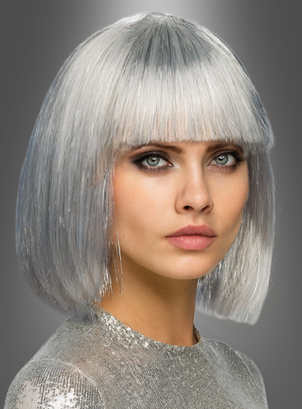 Eine Frau mit einem eisigen silbernen Bob und einem geraden Pony, die ein glänzendes silbernes Oberteil trägt und vor einem grauen Hintergrund mit Farbverlauf posiert – ein auffälliger Look mit der Perücke „Space Girl“ in Silber.