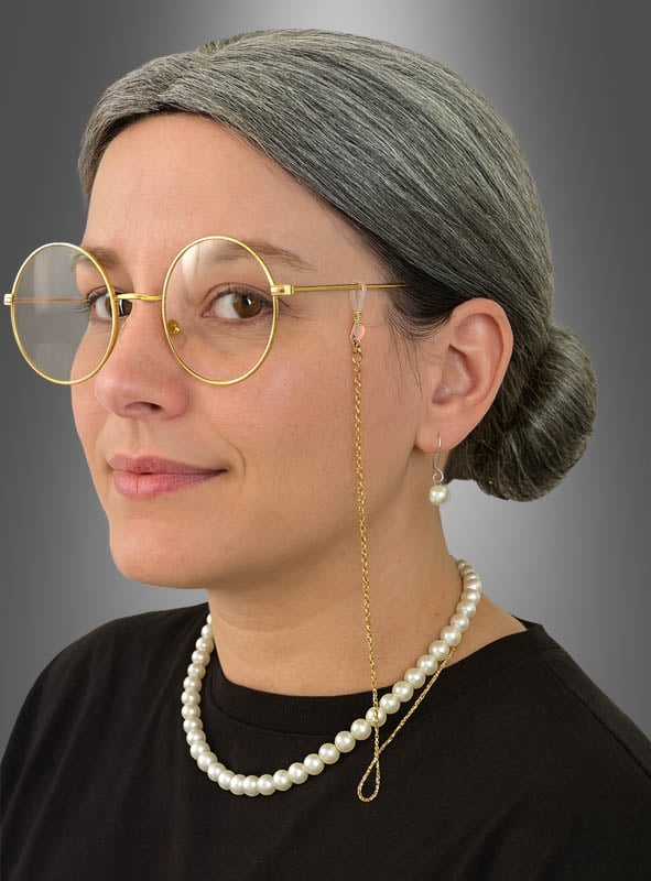 Eine Frau mit grauen Haaren, die zu einem Dutt frisiert sind, trägt das 6-teilige Set „Oma Dutt Perücke“ sowie eine runde Brille mit einer goldenen Kette, dazu eine Perlenkette, Perlenohrringe und ein schwarzes Oberteil; sie posiert vor einem grauen Hintergrund mit Farbverlauf.